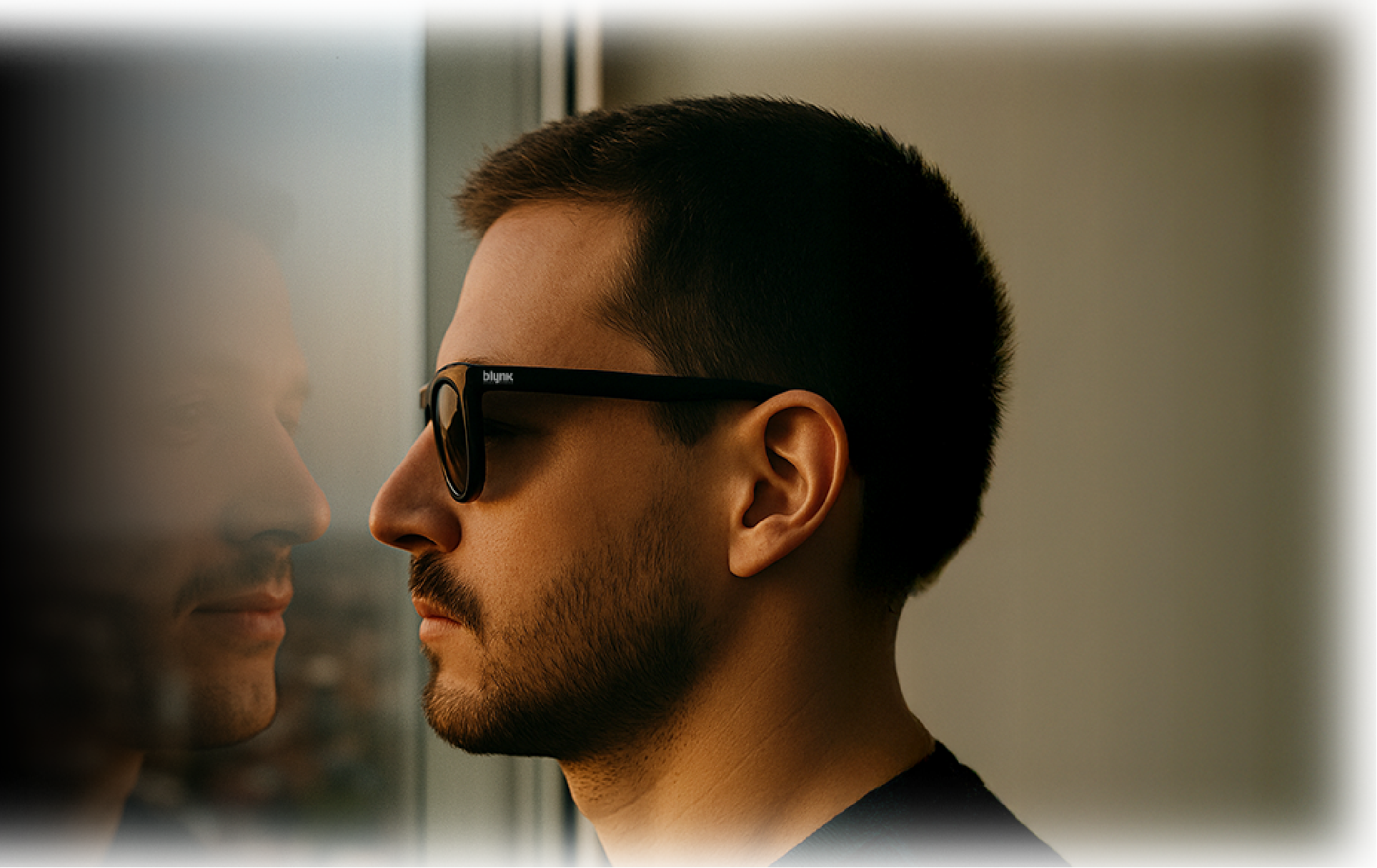 Hombre con lentes de sol viendo la ciudad a travez de una ventana y en su reflejo se ve sin lentes